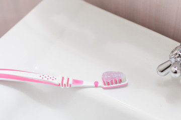 A pink toothbrush with a toothpaste is lying on the washbasin.