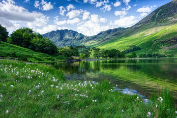 Landscape photography UK.Idyllic scenery of Lake District.Mountain lakeshore, trees  and green hills.Blue sky with few clouds above horizon.Trees and mountain reflection in water.