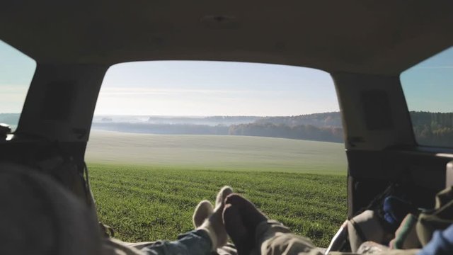 Personal perspective of couple lying in car's trunk, mountain landscape and admiring sunrise . Lovers alking and drinking hot coffee against backdrop of forest panorama in fog . View from inside 4k