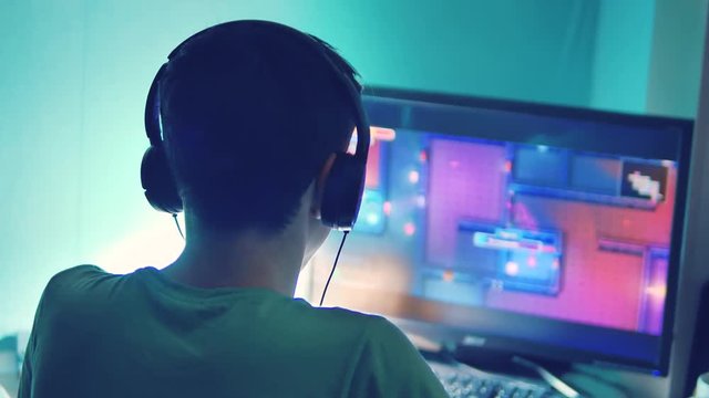 teen boy plays online game on computer via internet monitor in headphones. teenager man plays a video game at night lifestyle. teen boy and computer concept