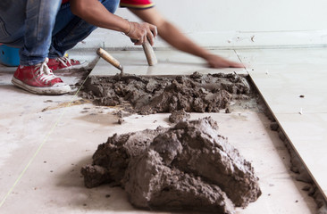 A construction worker putting tiles on the floor.Tiler installing ceramic tiles on a floor,Please note**Slightly Blurriness