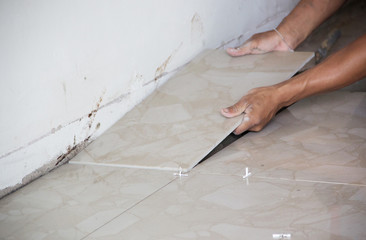 A construction worker putting tiles on the floor.Tiler installing ceramic tiles on a floor,Please note**Slightly Blurriness