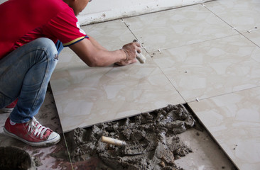 A construction worker putting tiles on the floor.Tiler installing ceramic tiles on a floor,Please note**Slightly Blurriness