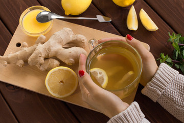 young woman making lemon and ginger root tea with honey on wooden cutting board