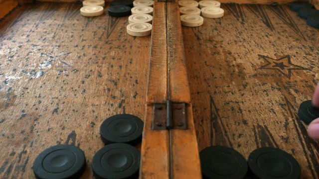 Two young men playing backgammon on a wooden table and move the piece.