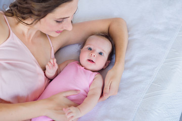 beautiful young mamma cuddling with her 4 months old baby girl on the bed