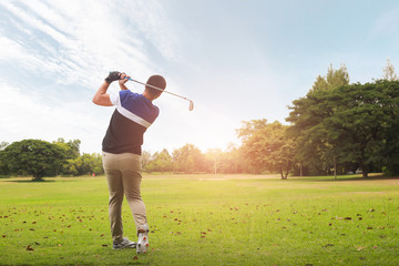 Golfer hitting golf shot with club on course at evening time.