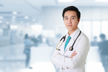 Doctor posing with arms crossed, medical staff working on blurry background.