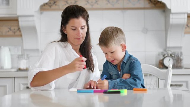 Beautiful mom and cute little son enjoying drawing picture together using multicolored felt-tip pen