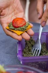 Woman hands making sandwich with homemade dehydrated crispy flat bread (flax bread with corn flour), pesto basil sauce and vegetables. Paleo diet, vegan snack, vegetarian healthy food