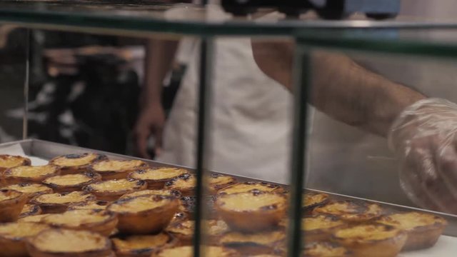 Traditional Portuguese egg hands take tart pasty cakes, dessert Pasteis de nata with different portuguese pastry on the cafe store window, pastel de nata