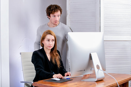 Portrait of young successful woman and man at office. They look at the display in surprise. Black Friday or Cyber Monday. Browsing or selecting items, making a deal, online shopping, good mood