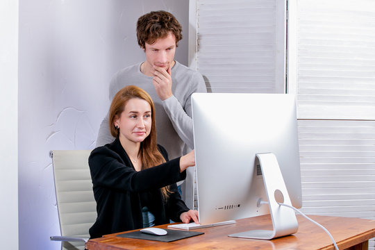 Portrait of young successful woman and man at office. They look at the display in surprise. Black Friday or Cyber Monday. Browsing or selecting items, making a deal, online shopping, good mood