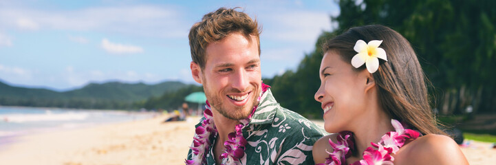 Hawaii tourists couple on beach vacation wearing lei necklace and flower for luau dance party....