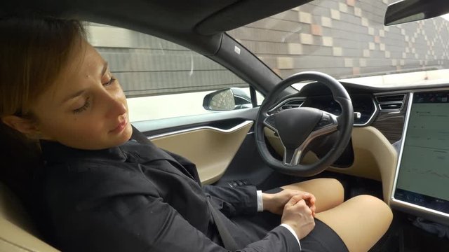 CLOSE UP: Caucasian businesswoman sleeping as the autonomous car drives her home. Tired young woman napping in her high tech self navigating vehicle after a business meeting. Relaxed stylish woman.