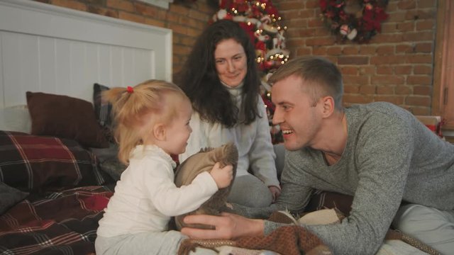 Christmas morning. The young family happily plays with each other. On the bed a lot of pillows, Christmas gifts in bright packaging and Christmas decorations. Merry Christmas 2019. Slow motion. 4K