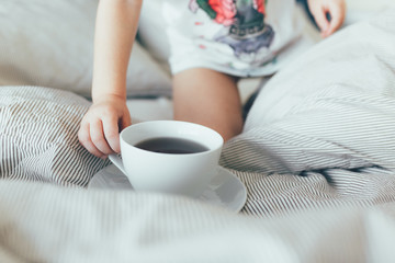 Bed maid-up with clean white pillows and bed sheets in beauty room. Morning breakfast with tea. Kid hold a cup. Close-up.