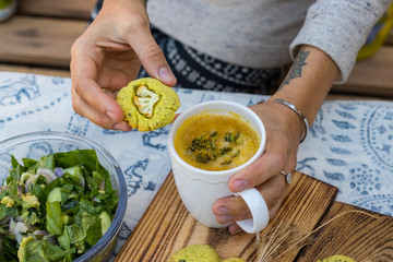 Woman hands holds hot broth vegetable soup in white cup with herbs, spices and greens. Fresh spinach avocado salad and corn turmeric bread with vegetables. Paleo vegan diet