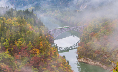 Fototapeta premium Train crossing the first bridge with surrounding beautiful autumn foliage and fog.