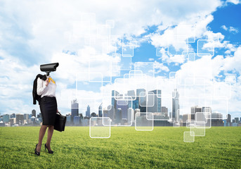 Camera headed woman standing on green grass against modern cityscape