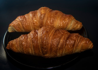 two fresh baked croissant on dark plate black background