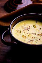 Basundi Or Rabri is an Indian sweet popular in Gujarat and Maharashtra. It is a sweetened condensed milk. Garnished with Dry fruits and Saffron. Served in a bowl over moody background. Selective focus