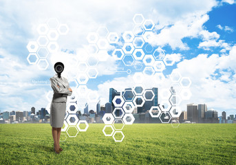 Camera headed woman standing on green grass against modern cityscape