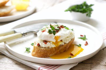 Crispy baguette toasts with cottage cheese, poached egg and dried tomatoes on a light background.