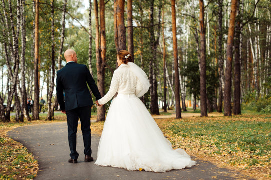 Portrait of an attractive groom and bride walking back on nature in the park. Romantic wedding moment, couple of newlyweds smiling portrait