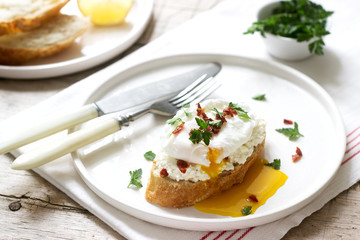 Crispy baguette toasts with cottage cheese, poached egg and dried tomatoes on a light background.