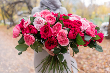 Big luxury bright bouquet in the hands of a cute girl. One hundred garden roses, varieties of David Austin. Three kinds of bright pink, scarlet and pastel colors. Autumn leaves in the Park.