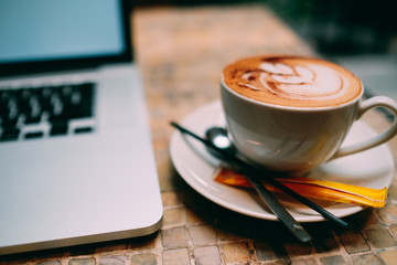 A cup of cappuccino coffee with laptop on table. Royalty high quality free stock image of capuccino coffee with laptop for working in a coffee shop. Beautiful workspace with retro and vintage style  