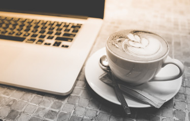 A cup of capuchino coffee or latte coffe in a white cup with laptop on table. Royalty high quality free stock photo of drink capuchino or latte coffe with laptop for working in office