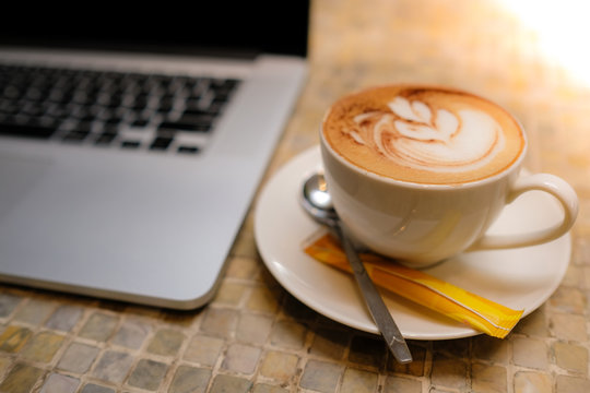 A cup of capuchino coffee or latte coffe in a white cup with laptop on table. Royalty high quality free stock photo of drink capuchino or latte coffe with laptop for working in office