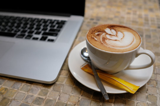 A cup of cappuccino coffee with laptop on table. Royalty high quality free stock image of capuccino coffee with laptop for working in a coffee shop. Beautiful workspace with retro and vintage style