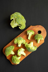 Raw broccoli on rustic wooden board on black background, overhead view. Flat lay, from above.