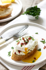 Crispy baguette toasts with cottage cheese, poached egg and dried tomatoes on a light background.