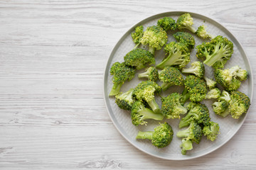 Freshly cut raw broccoli on gray plate on white wooden background, overhead view. Flat lay, from above, top view. Copy space.