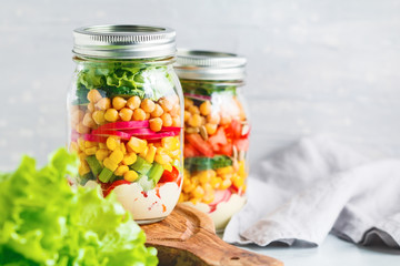 Fototapeta na wymiar Glass jars with layering various vegan salads for healthy lunch. The concept of fitness and vegetarian food.