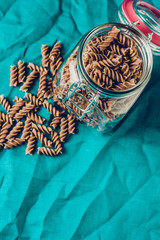 Dark brownwhole grains of pasta in a glass jar in the kitchen on a blue linen cloth - top view