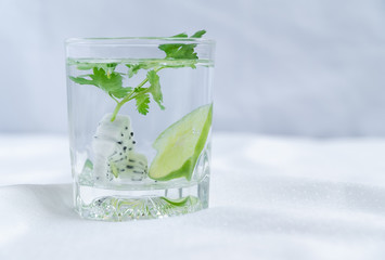 Close up view and copy space of detox water recipe. Which is coriander leaves with lemon slice in a glass. Placed on white cloth floor.