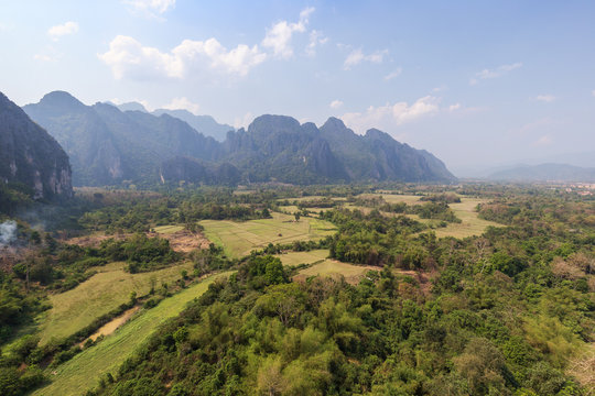 Beautiful view of fields and karst limestone mountains from above near Vang Vieng, Vientiane Province, Laos, on a sunny day.