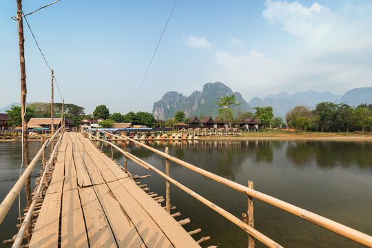 Limestone mountains, wooden bridge, empty waterfront restaurant, bungalows and Nam Song River in Vang Vieng, Vientiane Province, Laos, on a sunny day.