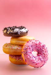 Pile of colorful donuts on pink background.