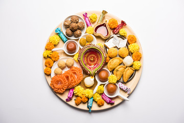Diwali sweets arranged in a plate with diya and flowers