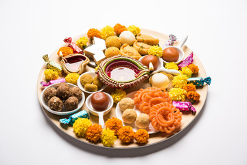 Diwali sweets arranged in a plate with diya and flowers