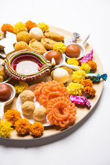 Diwali sweets arranged in a plate with diya and flowers