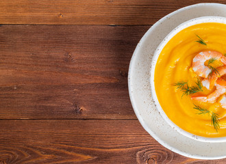 Half part of delicious pumpkin cream soup with shrimp on dark brown wooden background, top view, copy space