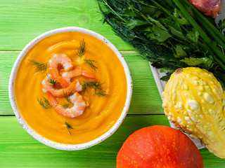 Delicious yellow pumpkin cream soup with shrimp and vegetables on bright green wooden table, top view