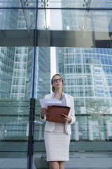 The young business woman in gray office dress holds in hand folder with documents. Businesswoman standing next to the business center